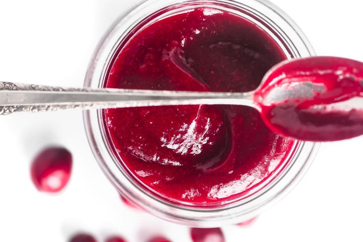 a spoon with some food in it on top of a glass jar filled with cranberry sauce