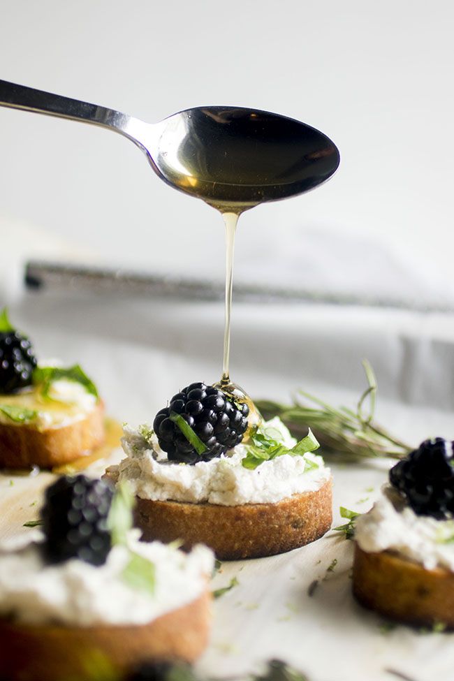 a spoon drizzling olives onto small appetizers with whipped cream and blackberries