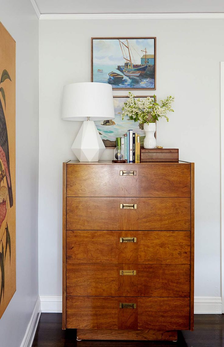 a wooden dresser with two lamps on top of it next to a painting and lamp shade