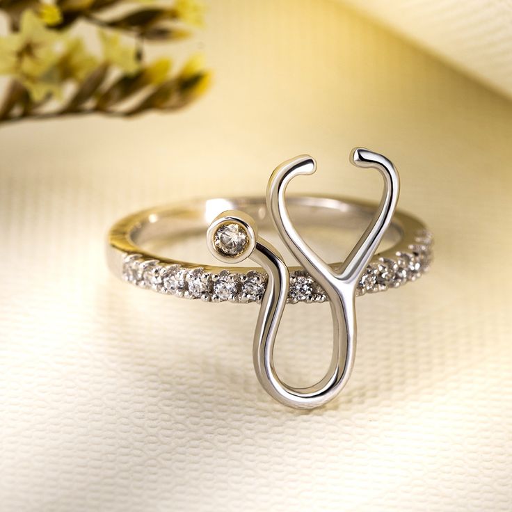 a white gold ring with diamond accents and a heart shaped design on the side, sitting next to a flower