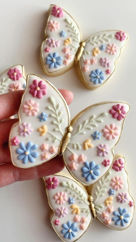 three decorated cookies in the shape of butterfly's wings are being held by a hand