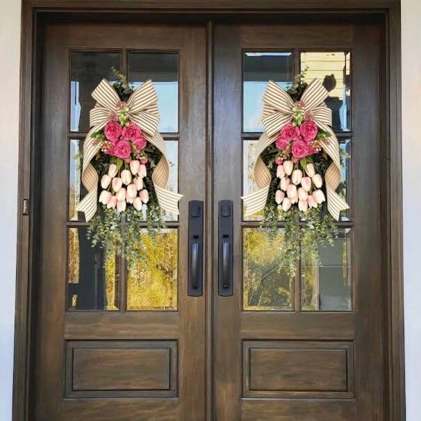 two brown double doors with wreaths and flowers on the front door to a house