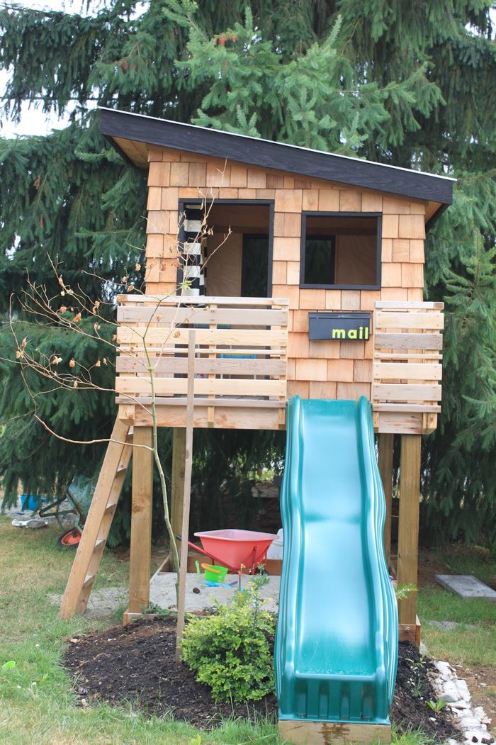 a small wooden house with a slide in the yard