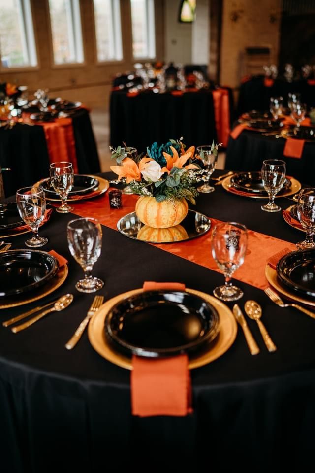 the table is set with black and gold plates, silverware, and orange napkins