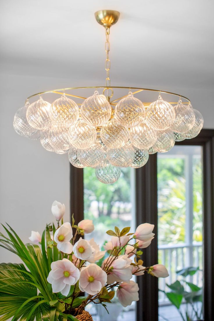 a chandelier hanging over a dining room table with flowers in the vases