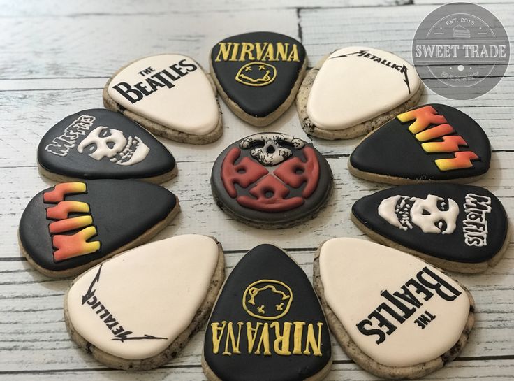 nine decorated cookies arranged in the shape of guitar picks with different logos and names on them