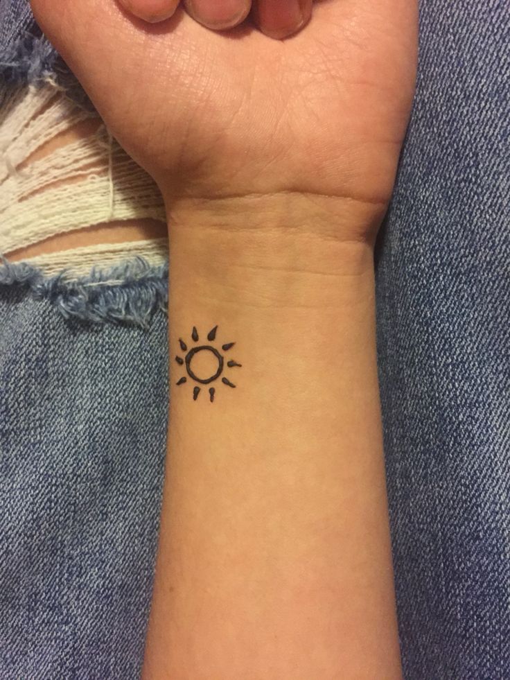 a woman's wrist with a small sun tattoo on the left side of her arm