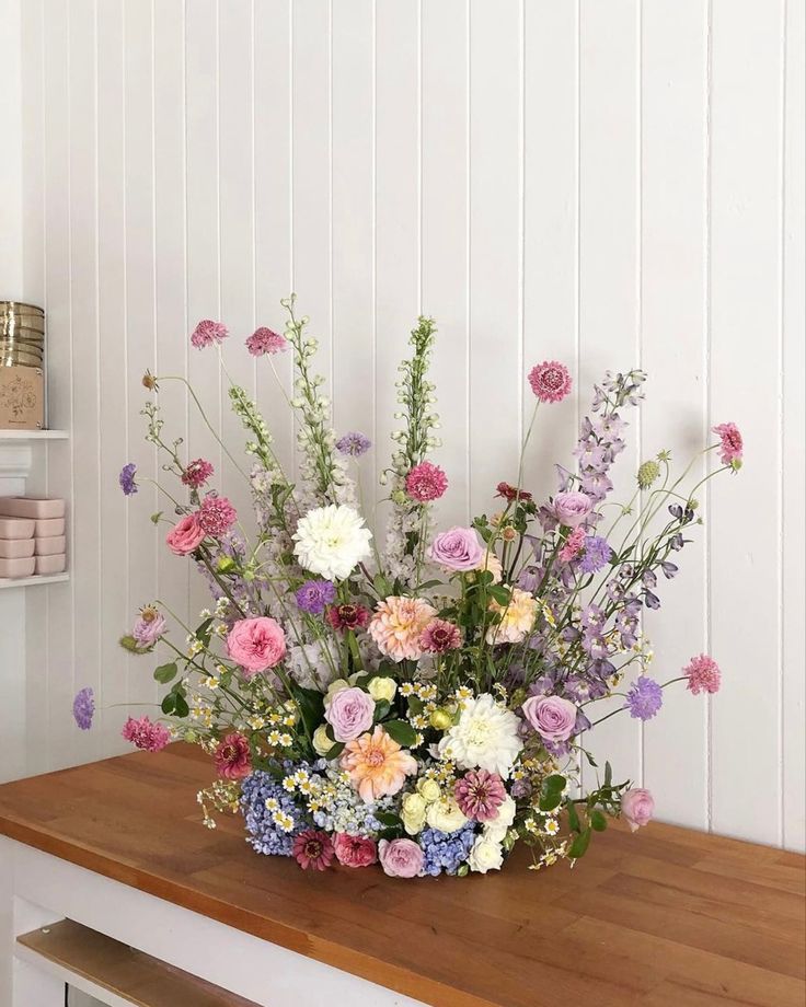 a vase filled with lots of flowers sitting on top of a wooden table next to a shelf