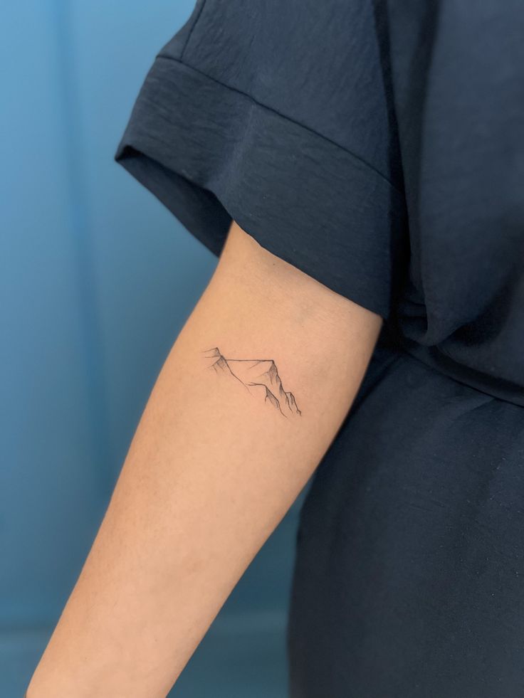 a woman's arm with a small mountain tattoo on the left side of her arm