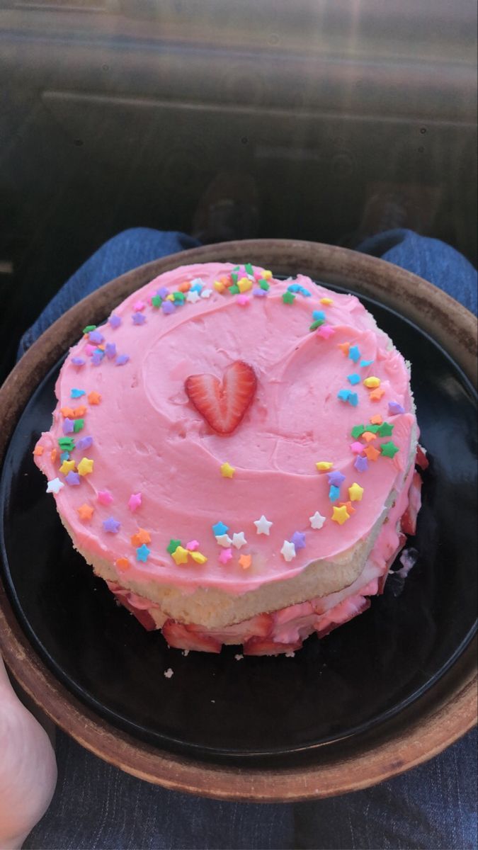 a pink frosted heart shaped cake on a black plate