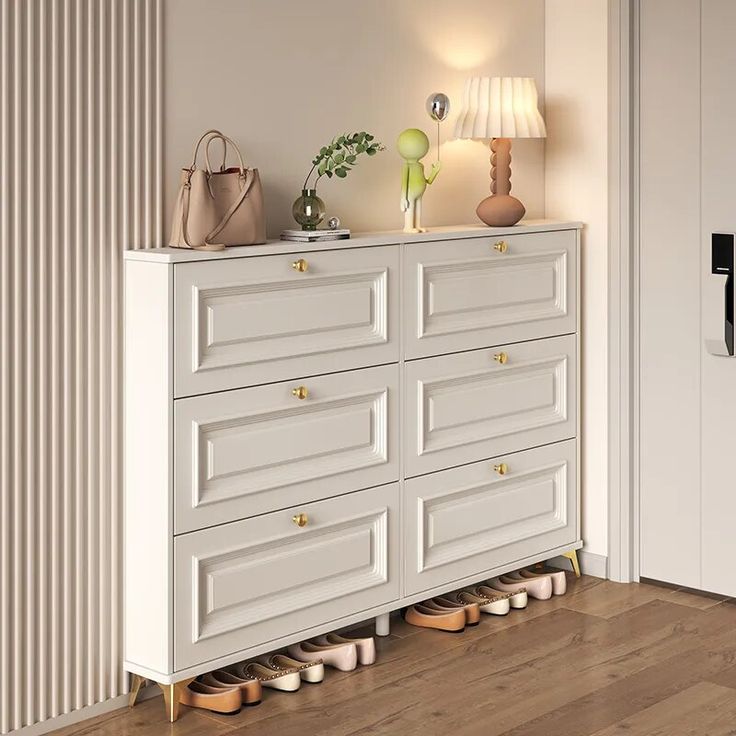 a white dresser with shoes on it in front of a door and a lamp next to it