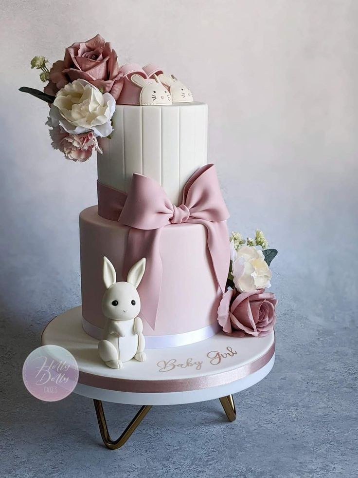 a three tiered cake decorated with pink flowers and bunny figurines on a stand