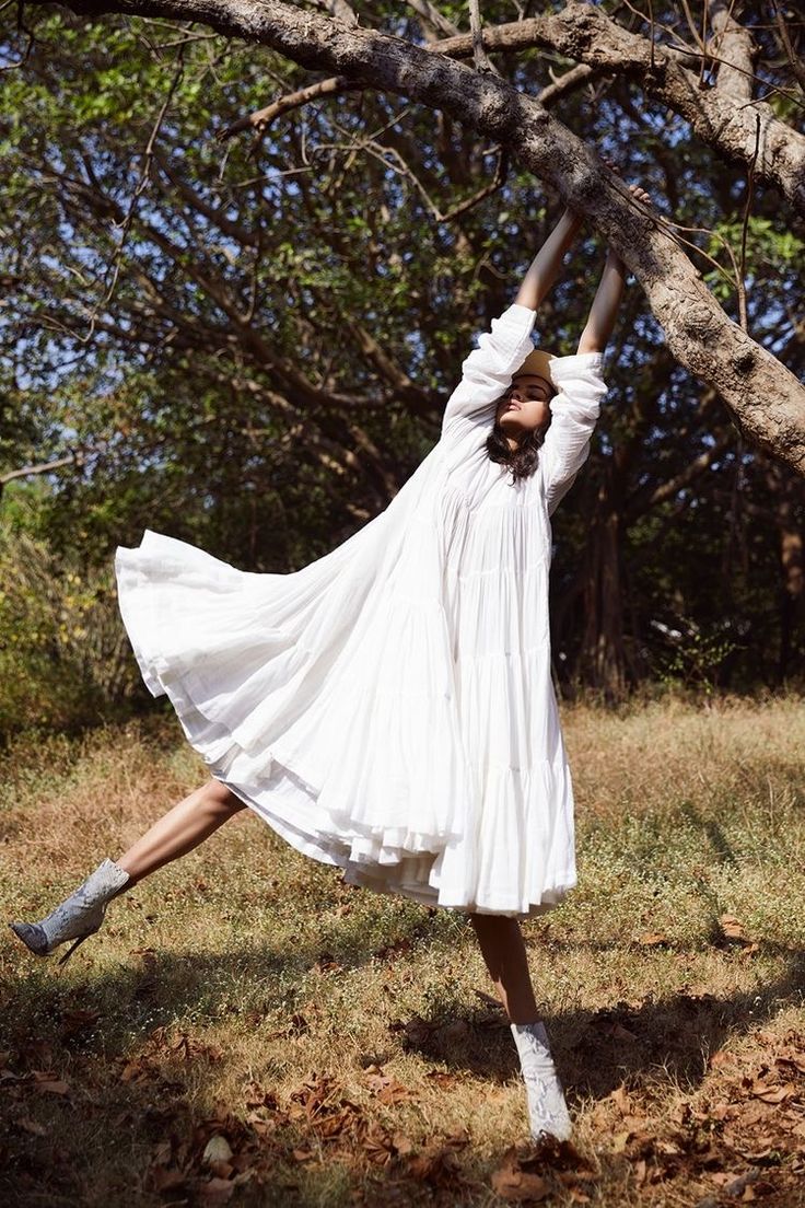 a woman in a white dress and boots is doing a handstand on a tree branch