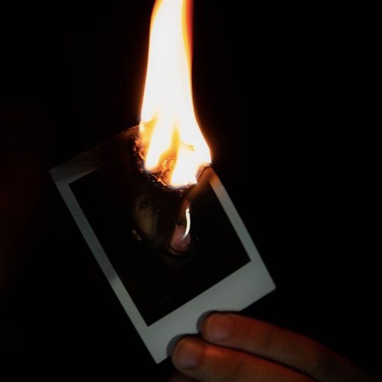 a person holding a polaroid in the dark with a fire coming out of it