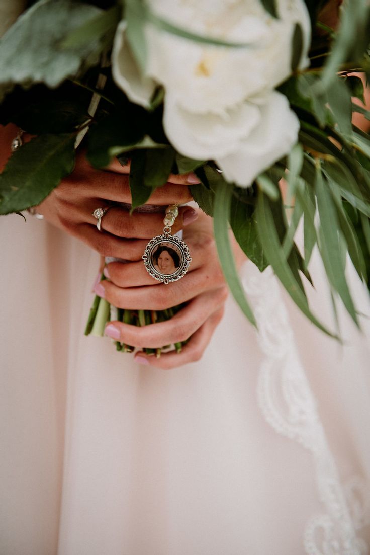 a woman in a wedding dress holding a bouquet with flowers on her arm and wearing a ring