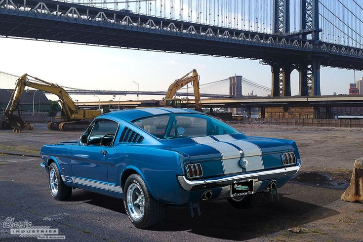 an old blue car is parked in front of a bridge and some construction equipment on the other side