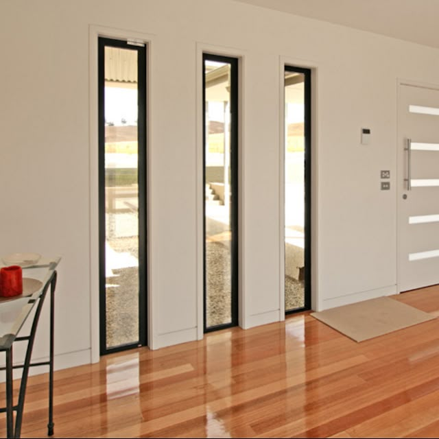 an empty room with wooden floors and white walls, has glass doors leading to the outside