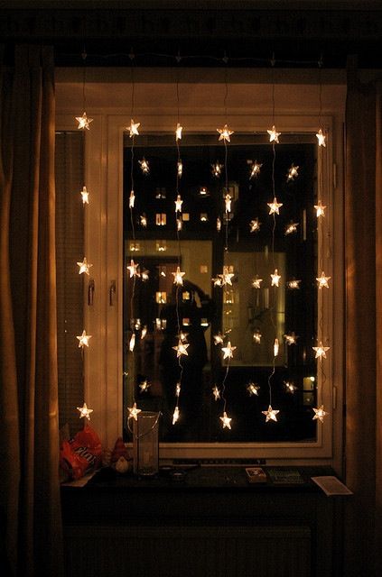 a window covered in white stars next to a curtained window sill with lights hanging from it