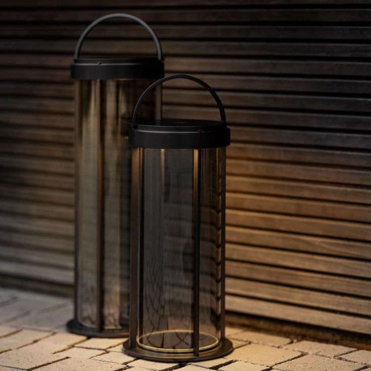 two black lanterns sitting next to each other on a brick floor in front of a building