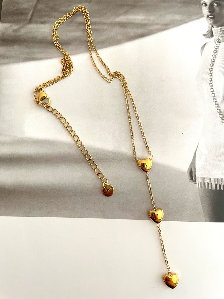 Rehaussez votre look avec ce collier lariat triple cœur. Fabriqué de manière experte en acier inoxydable et fini avec un placage or, il ajoute une touche de luxe moderne à n'importe quel ensemble. Avec trois cœurs, c'est le moyen idéal d'exprimer votre style et votre amour. Triple Heart, Three Hearts, Elevate Your Look, Lariat Necklace, Touch Of Modern, Modern Luxury, Gold Plating, Your Style, Gold Plate