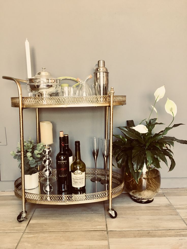 a gold bar cart with bottles and glasses on the counter next to a potted plant