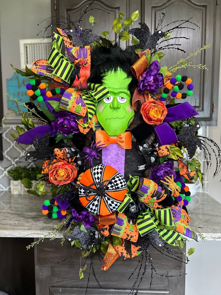 a halloween wreath with a green face and orange flowers on the front door for decoration