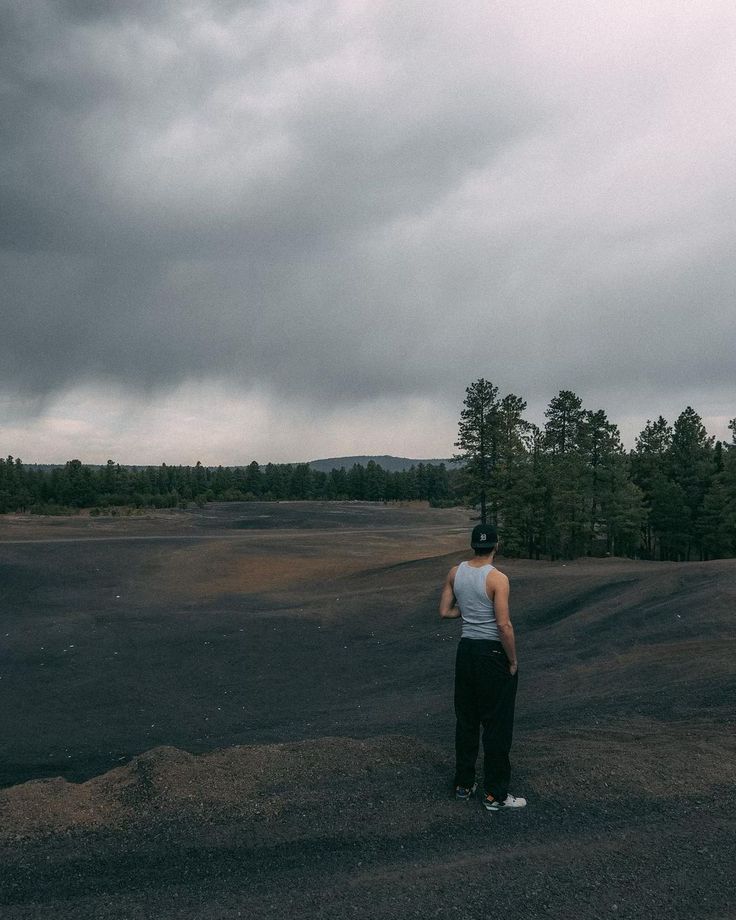 a man standing in the middle of an empty field under a dark sky with storm clouds