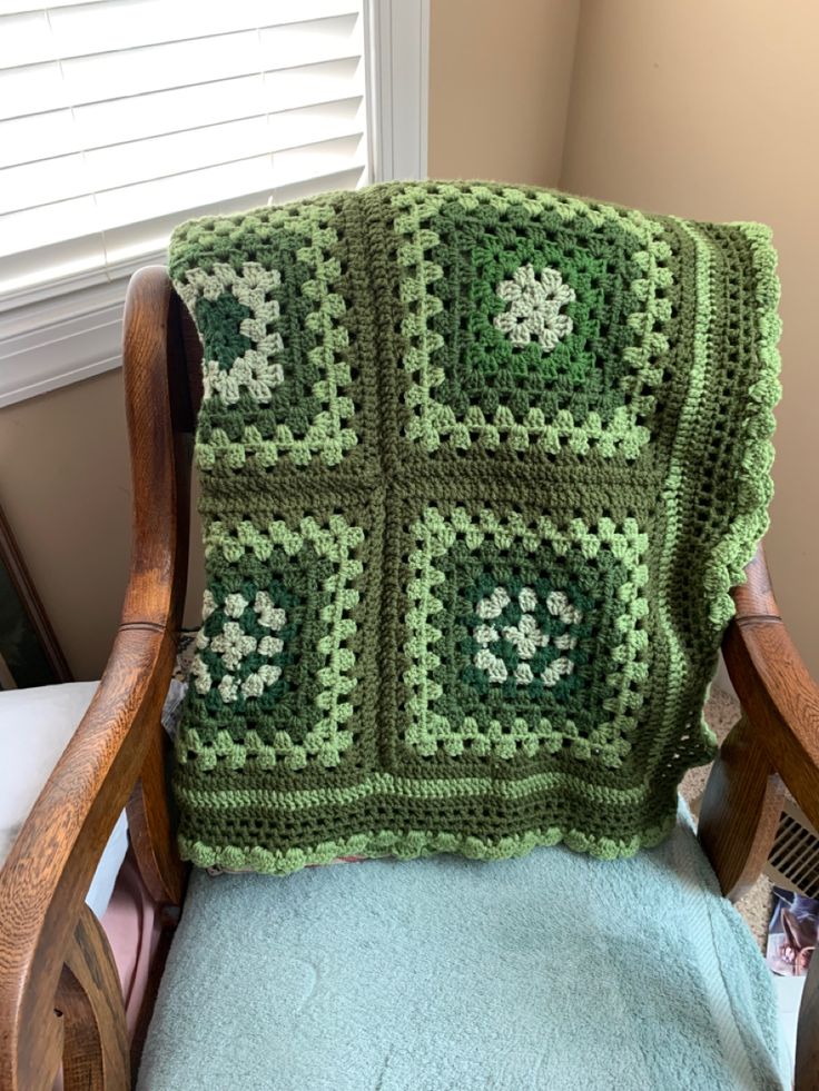 a green crocheted blanket sitting on top of a wooden chair next to a window