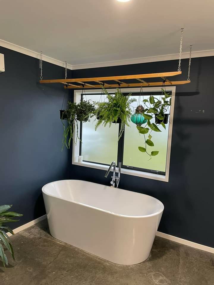 a white bath tub sitting under a window next to a green plant in a pot