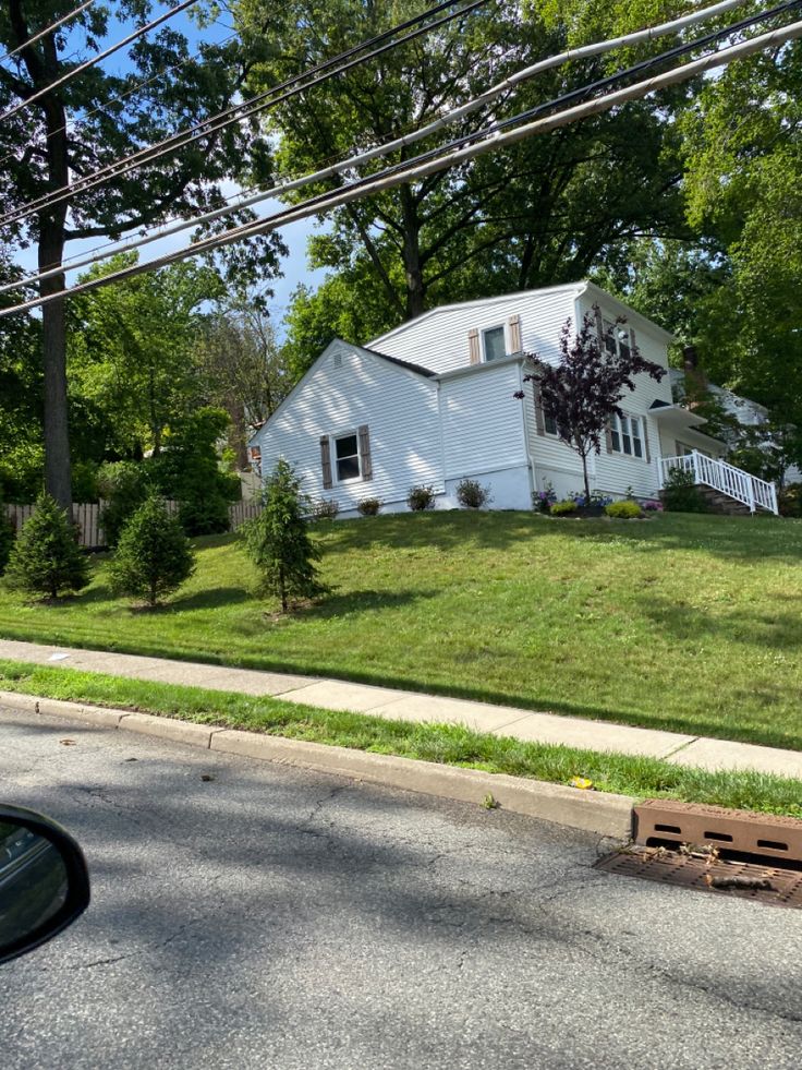 a white house sitting on the side of a road next to a lush green field