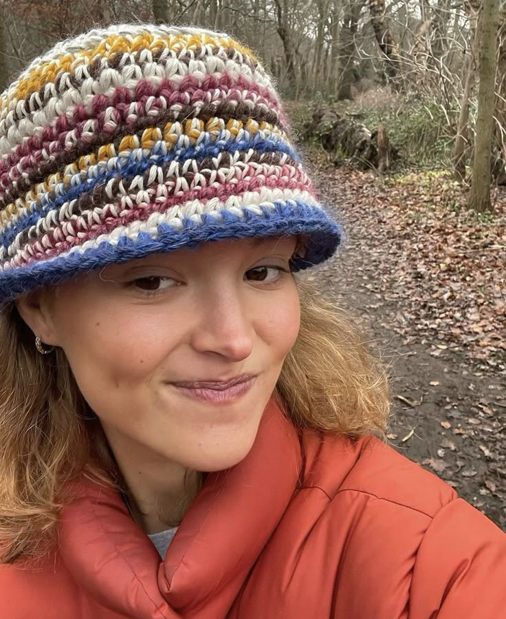 a woman in an orange jacket is wearing a multicolored hat and smiling at the camera