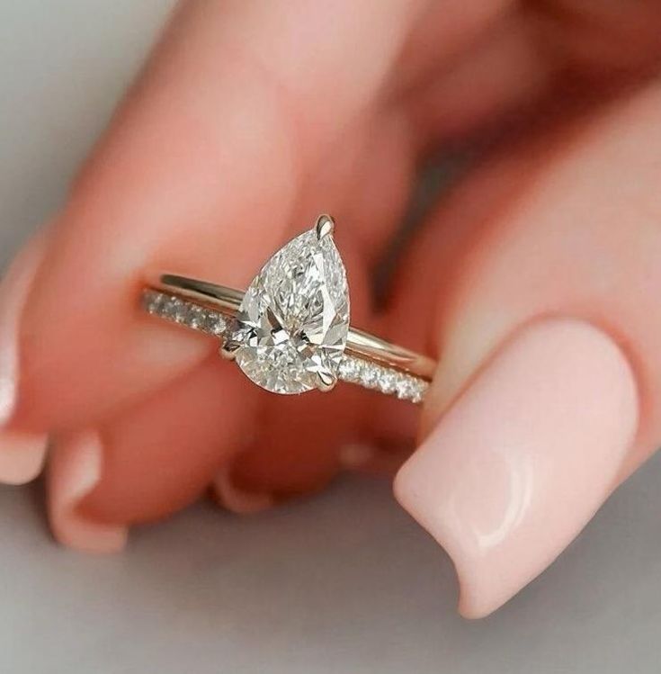 a woman's hand holding a ring with a pear shaped diamond on top of it