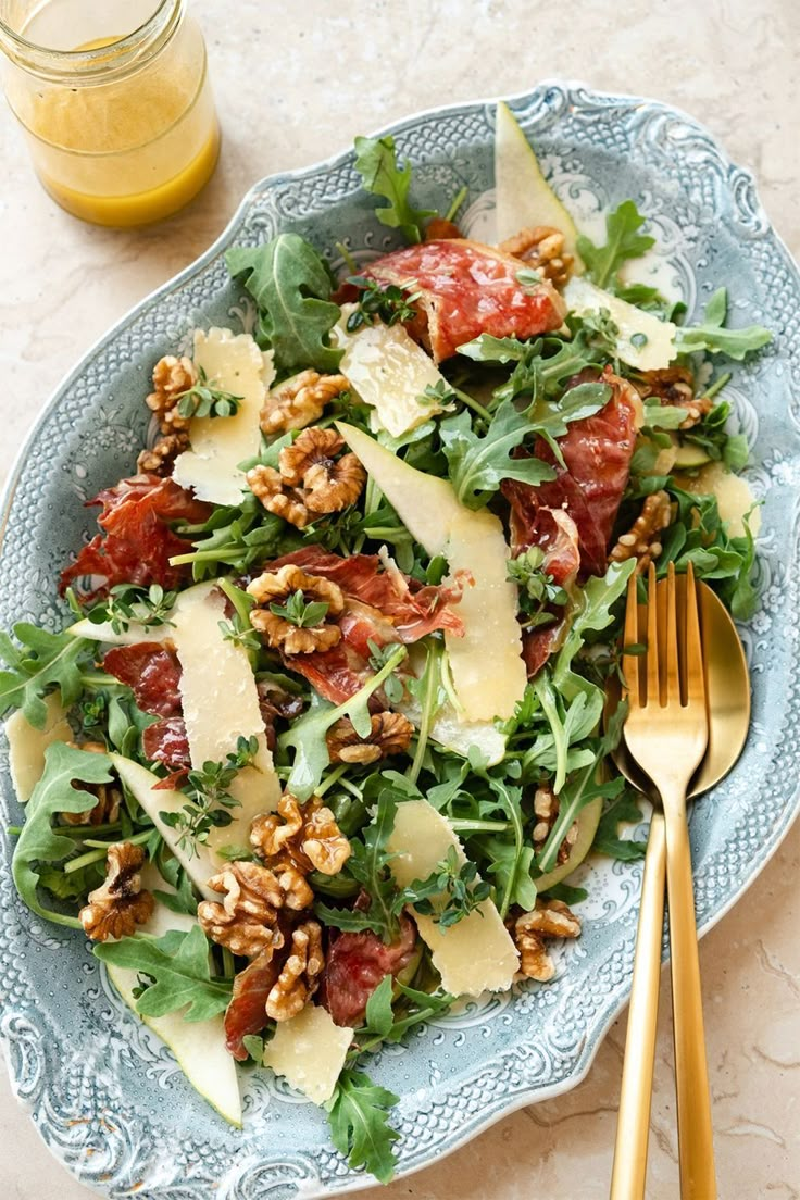 a salad with cheese, tomatoes and walnuts on a plate next to a glass of orange juice