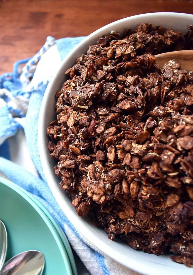 a white bowl filled with granola on top of a blue towel next to spoons