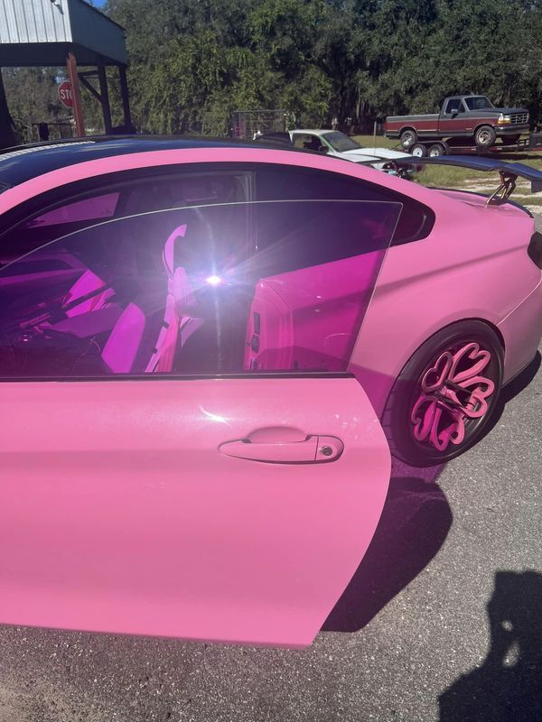 a pink car parked in a parking lot with its door open and the window partially closed