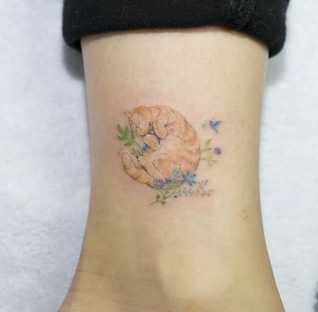 a cat tattoo on the ankle with blue flowers