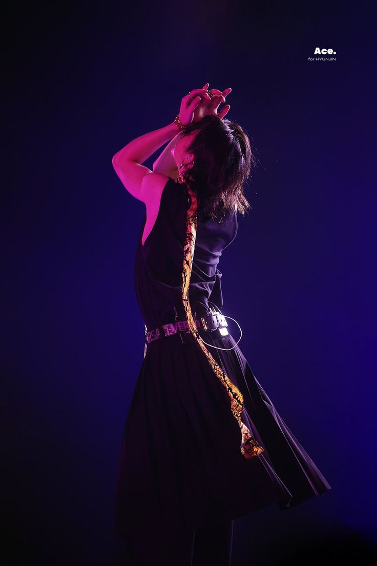 a woman in a black dress on stage with her hand up to her head and wearing a gold chain around her neck