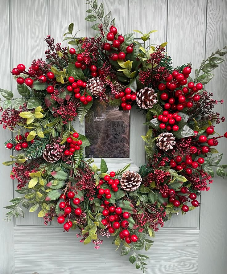 a wreath with red berries, pine cones and green leaves on the front door frame