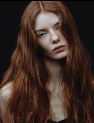 a woman with long red hair standing in front of a black background and looking at the camera