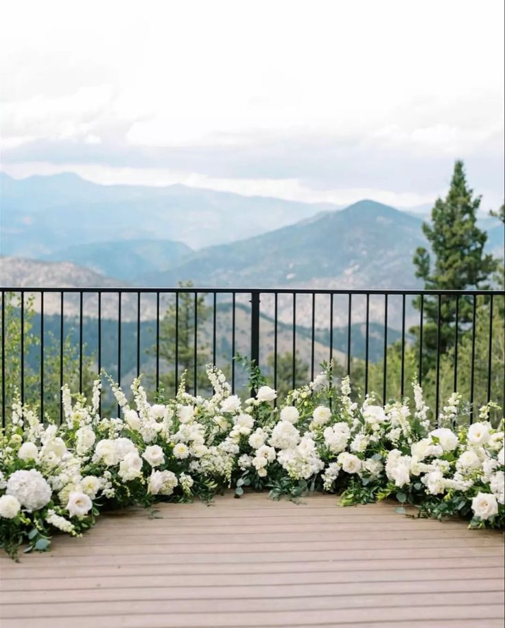 white flowers are arranged in the middle of a wooden deck with mountains in the background