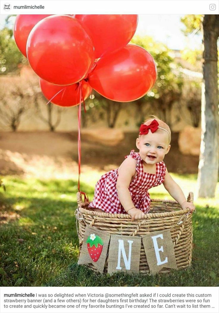 a baby sitting in a basket with red balloons attached to the handle and name on it