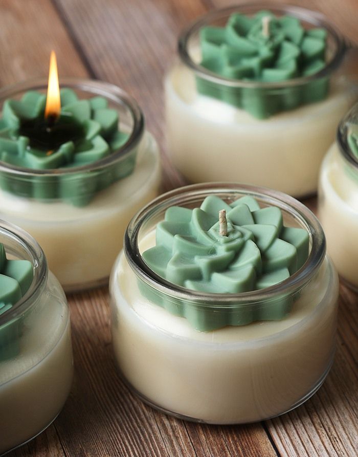 four candles are sitting in small glass containers on a table, one is green and the other is white