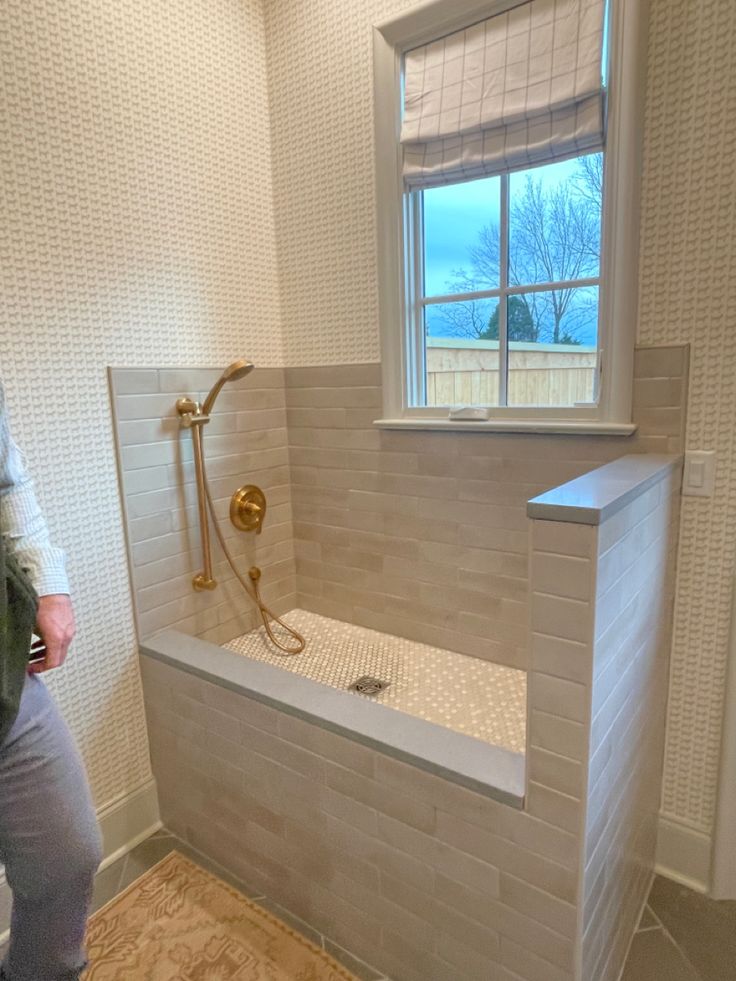 a man standing in front of a window next to a bathtub and shower head