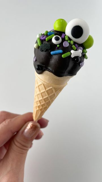 a hand holding an ice cream cone decorated with googly eyes and green sprinkles