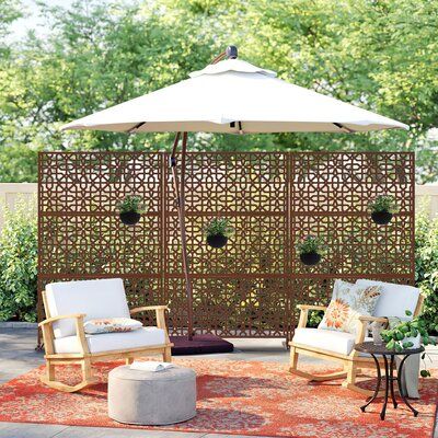 an outdoor seating area with chairs, umbrella and rugs on the ground in front of trees