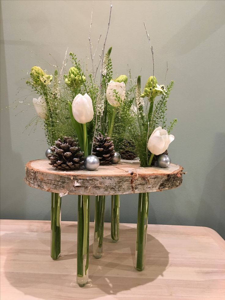 some white flowers are sitting on top of a wooden table with pine cones and greenery