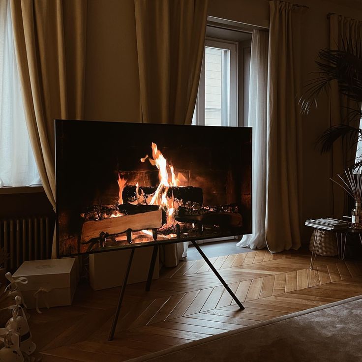 a large television with a fire burning in it's fireplace next to a window