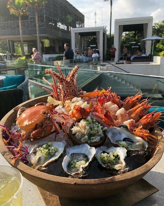 a wooden bowl filled with assorted seafood on top of a table next to a swimming pool