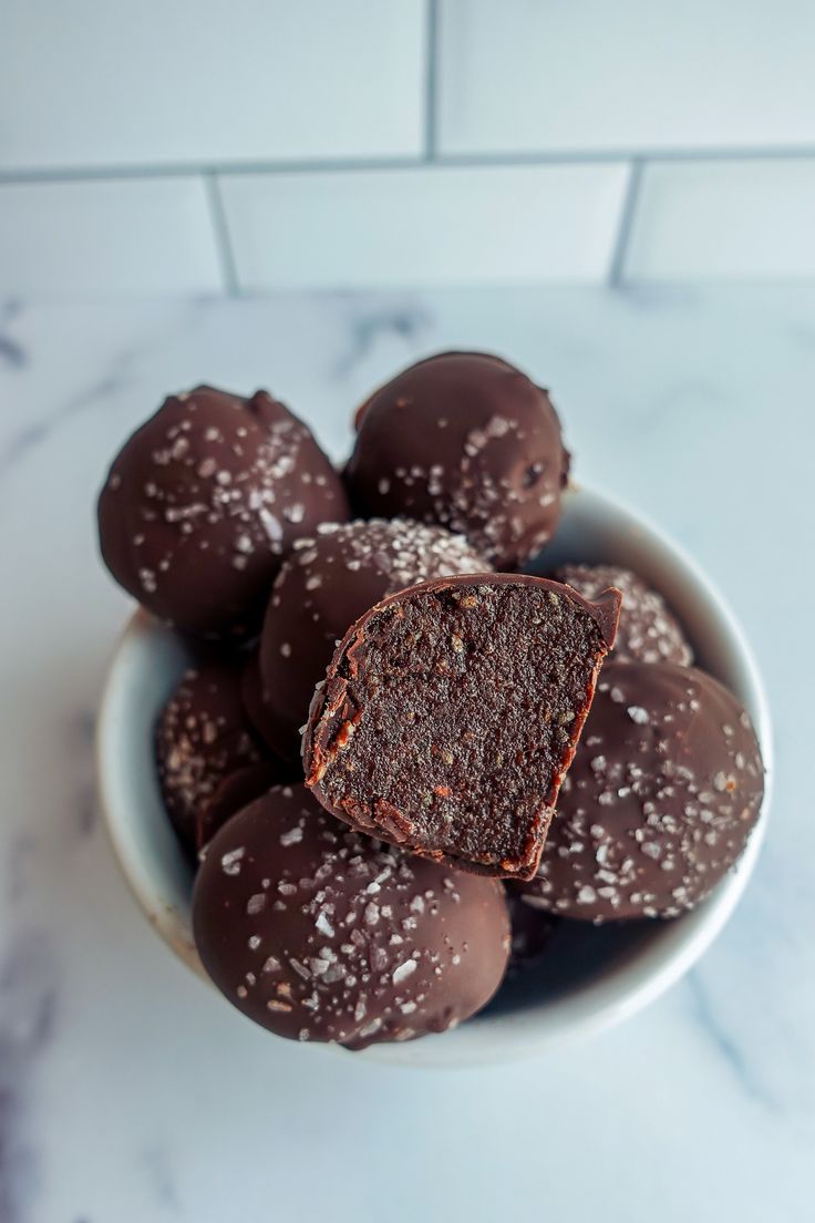 a white bowl filled with chocolate truffles on top of a marble countertop