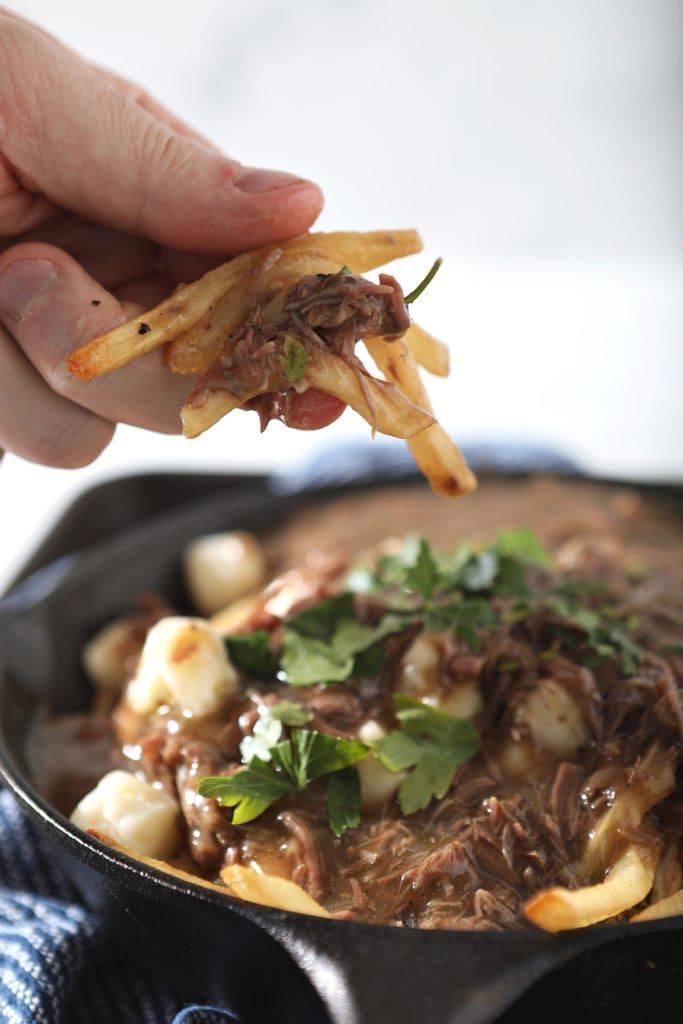 a person is dipping some food into a skillet with meat and cheese on it